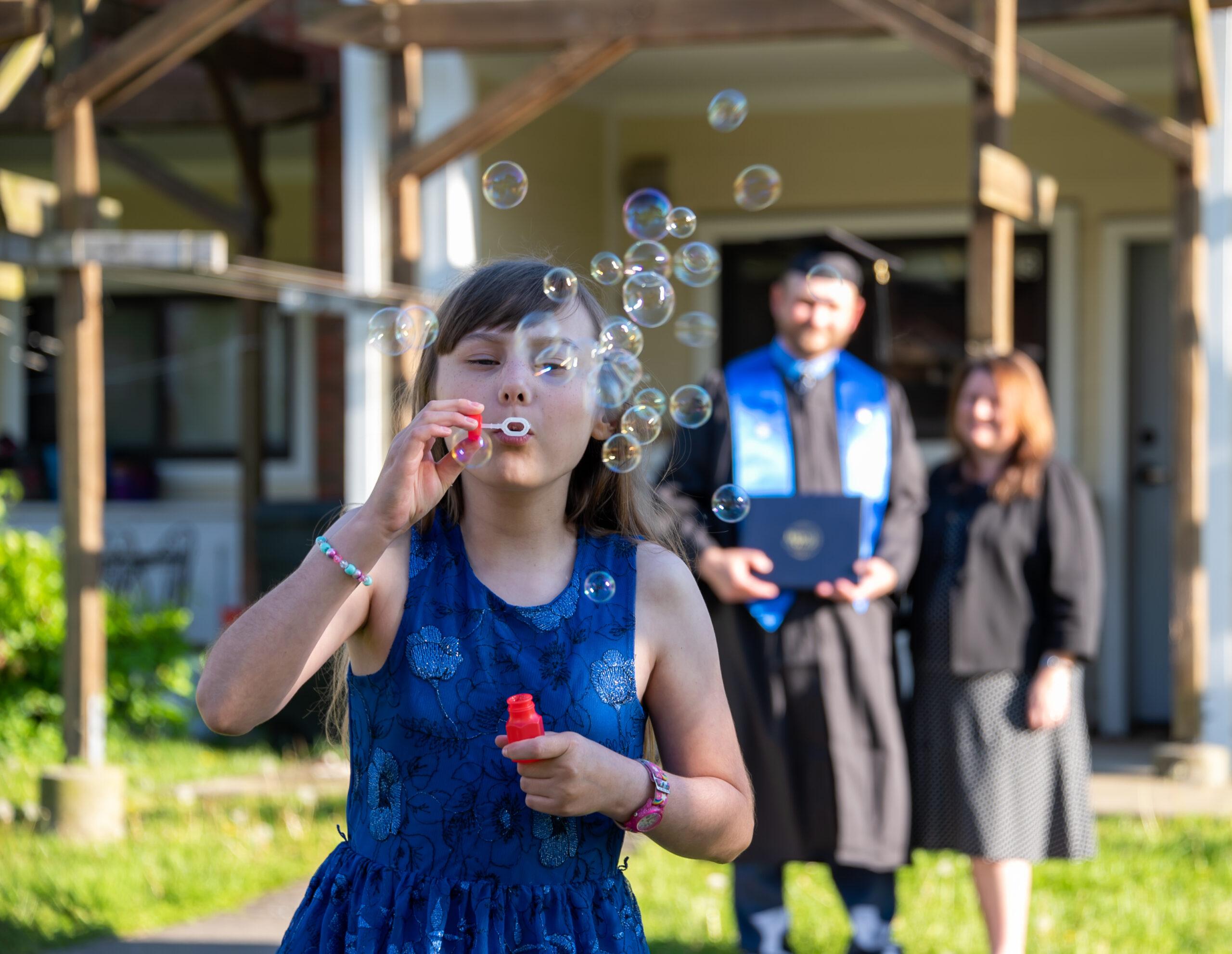 Student parents and child blowing bubbles at Berea College graduation.